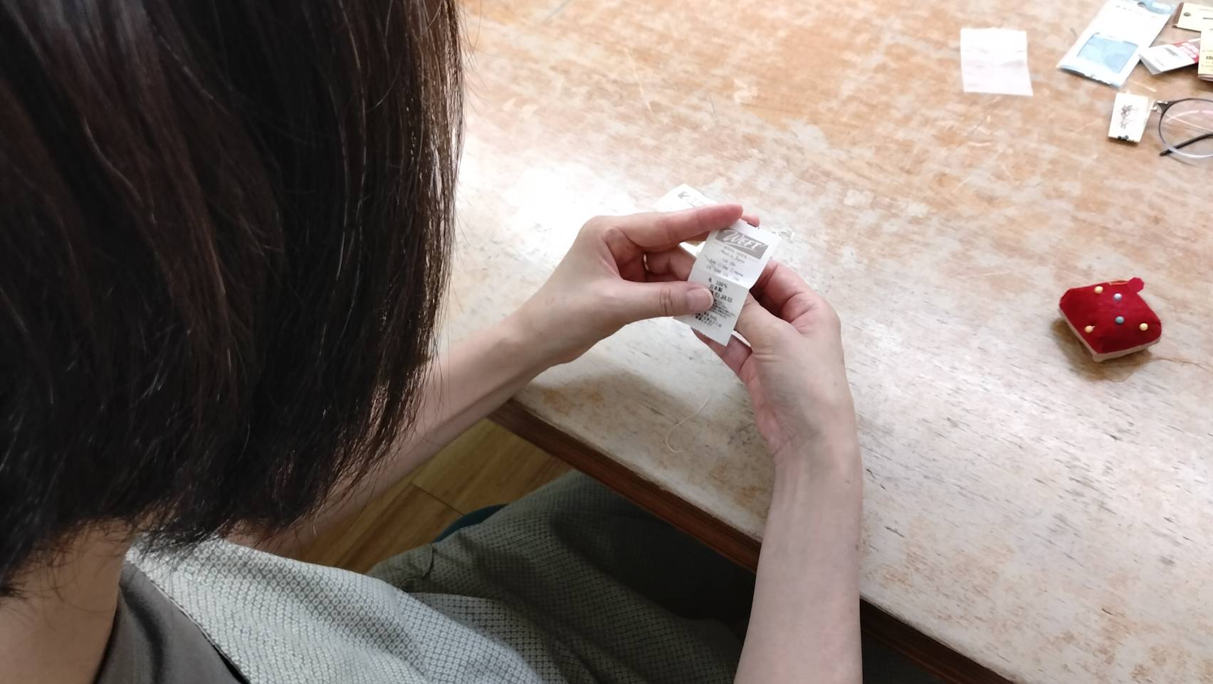WEFT のネームタグを取り付ける手元の様子。ミシン、はさみ、ピンクッションが机に並ぶ。