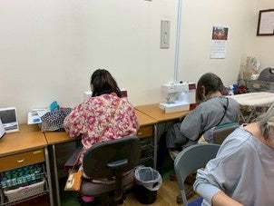 就労支援事業所(B型)で複数の方々が並んで作業している様子。後ろ姿で撮影。